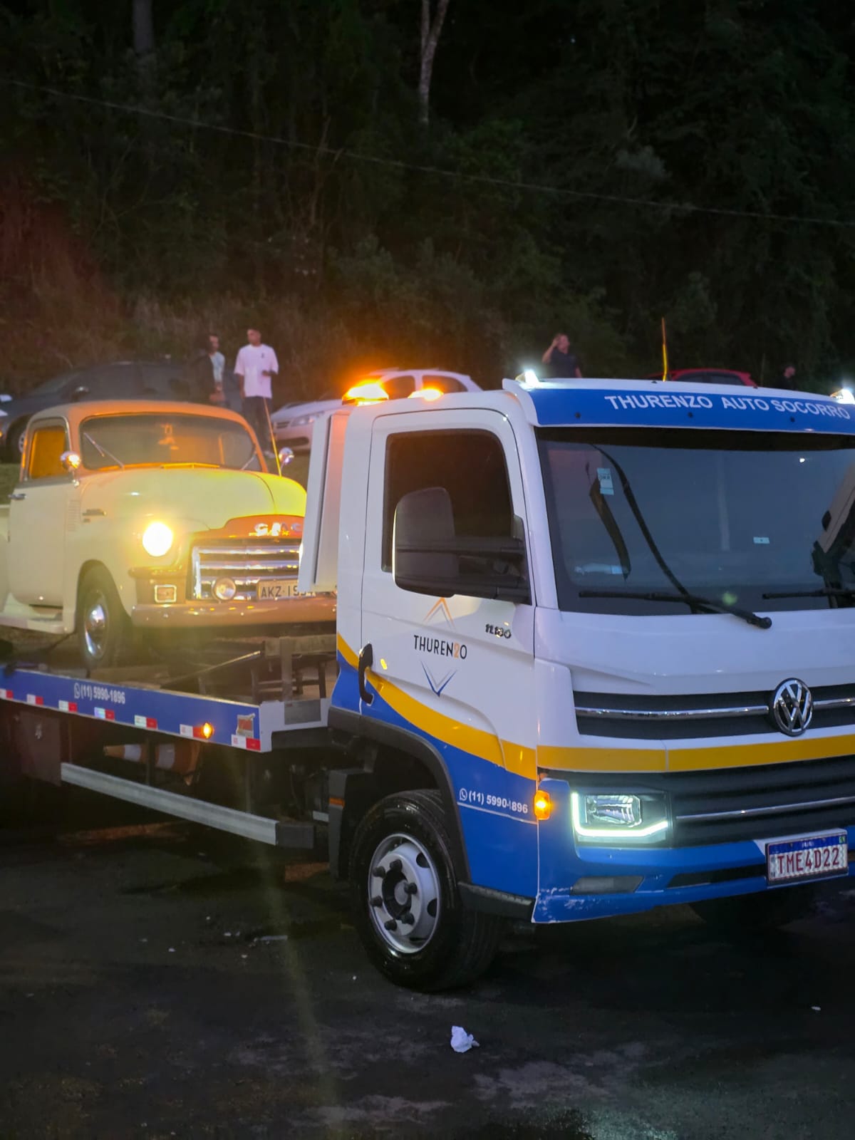 Caminhão plataforma Thurenzo transportando veículo clássico à noite